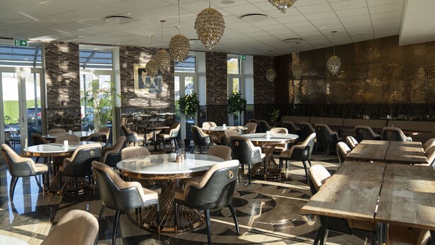 A spacious indoor dining area with multiple tables and chairs, large windows, and decorative crystal chandeliers. - A Hotels Glostrup (Brondby)