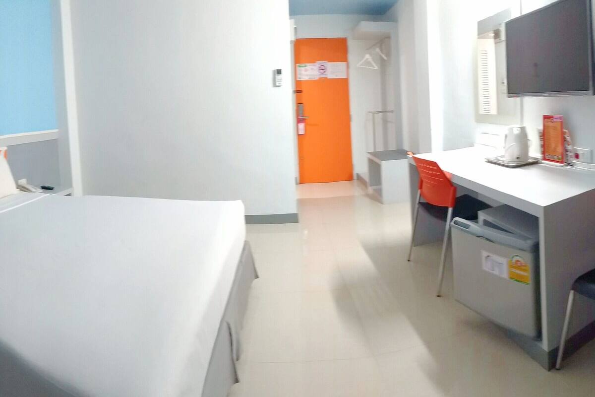 A hotel room with a bed, a desk, a chair, a television, and a door.