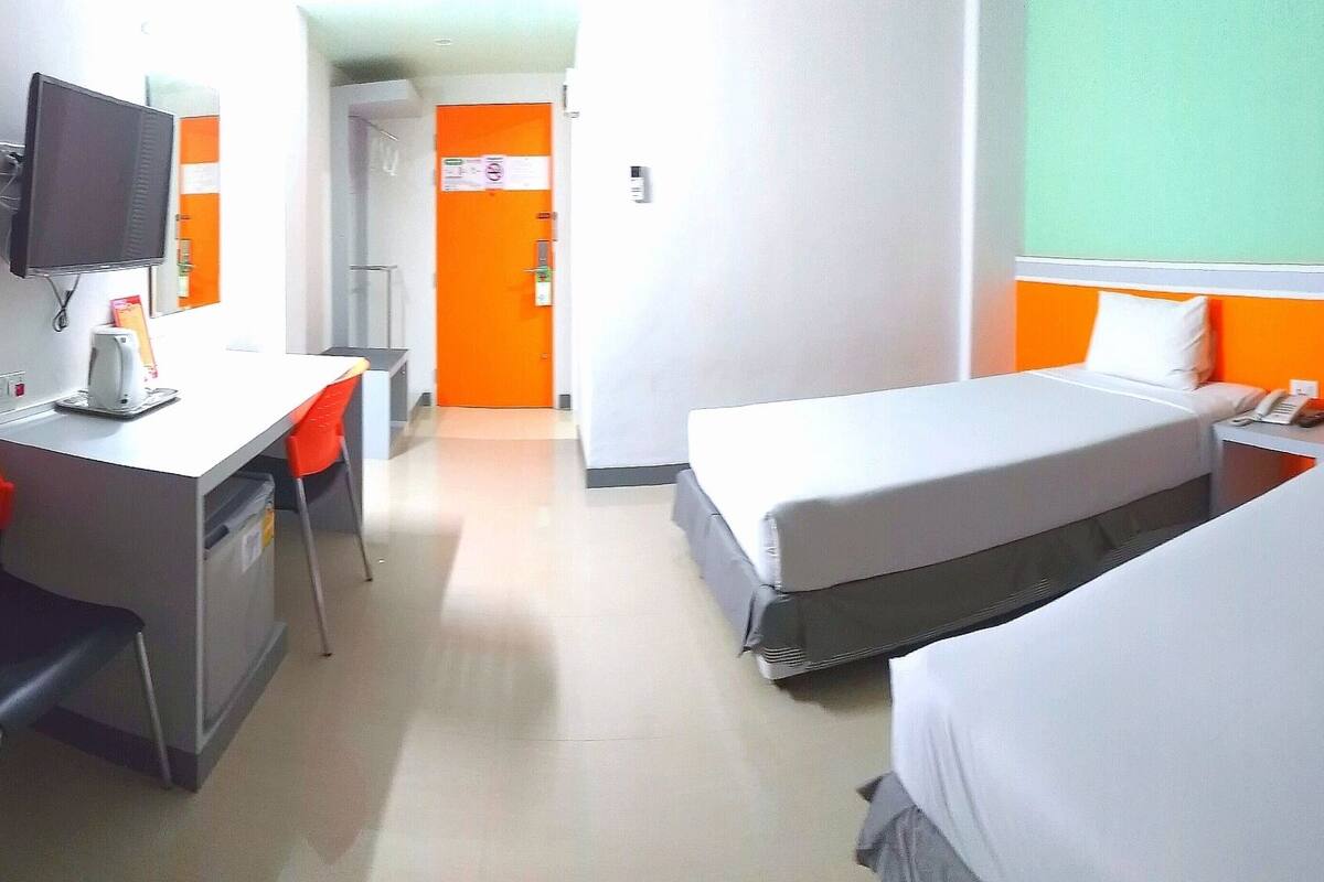 A hotel room with two beds, a desk, a chair, a television, and a bathroom visible in the background.