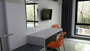 A modern room with a desk, two chairs, a flat-screen TV, and a large window with a view of trees. - Sakura Budget Hotel (Hat Yai)