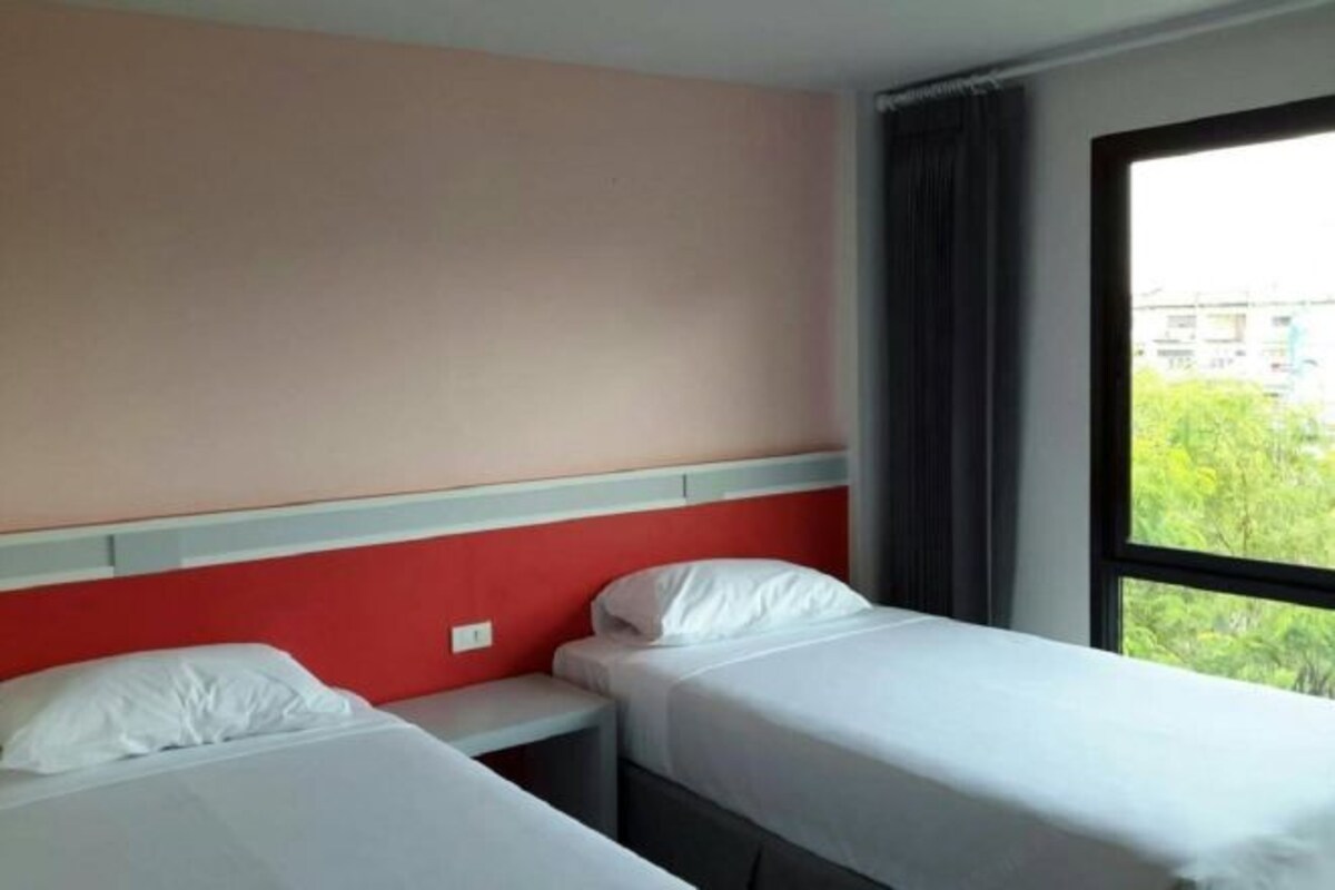 A hotel room with two single beds, a window with a view of greenery, and a red accent wall.
