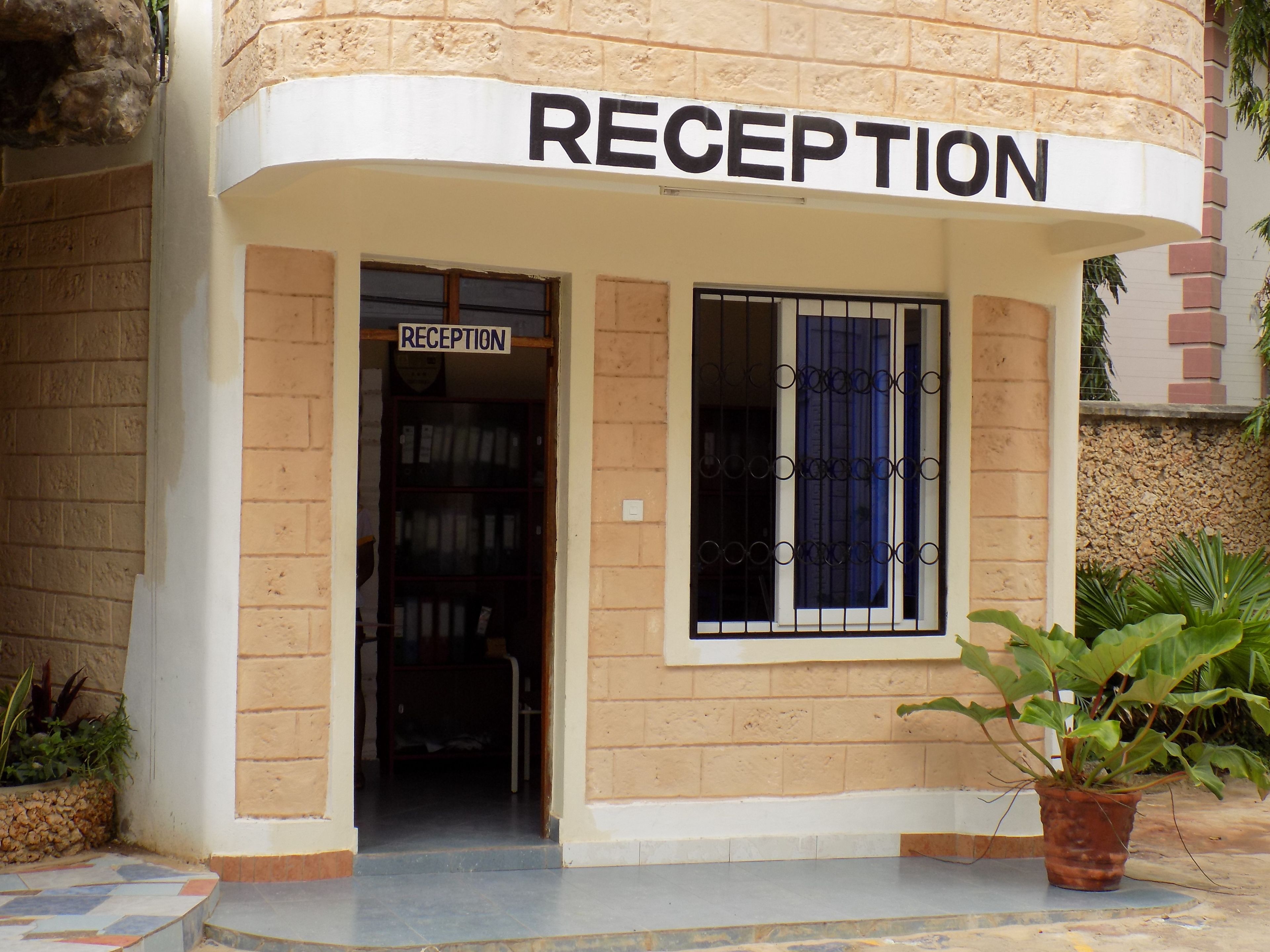 A reception area with a sign above the door, a window with metal bars, and a potted plant outside.
