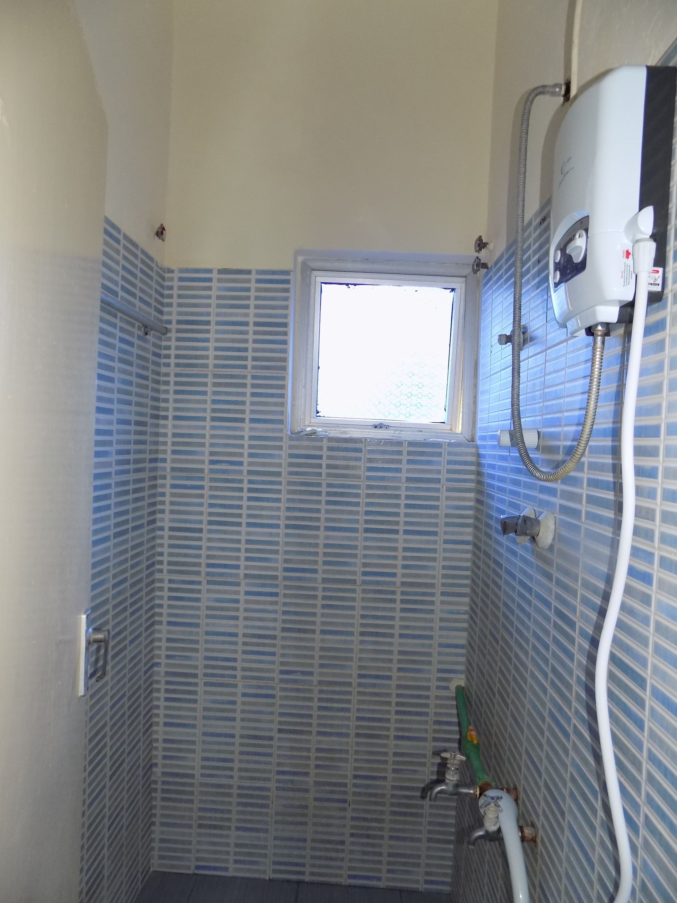 A bathroom with blue-tiled walls, a window, a showerhead, and a water heater.