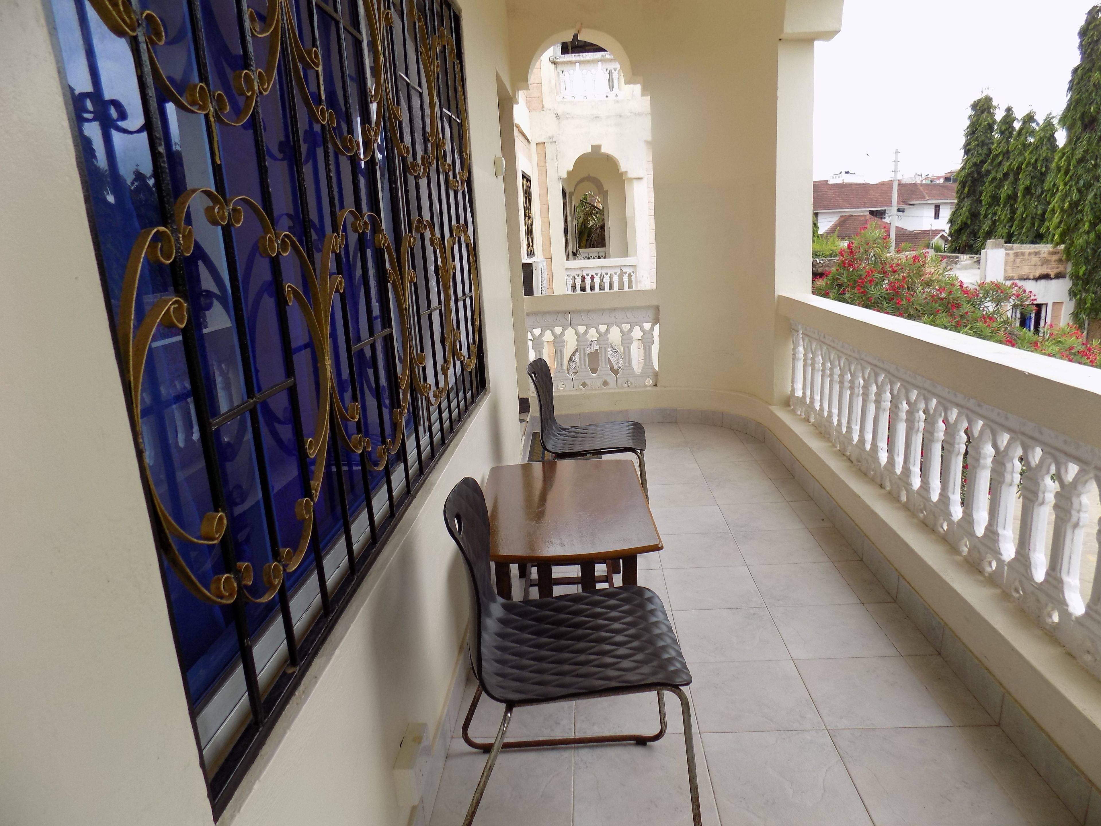 A balcony with a table and chairs, a decorative metal gate, and a view of a building with an archway.