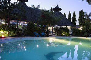 Una piscina con una estructura de techo de paja y palmeras al fondo.