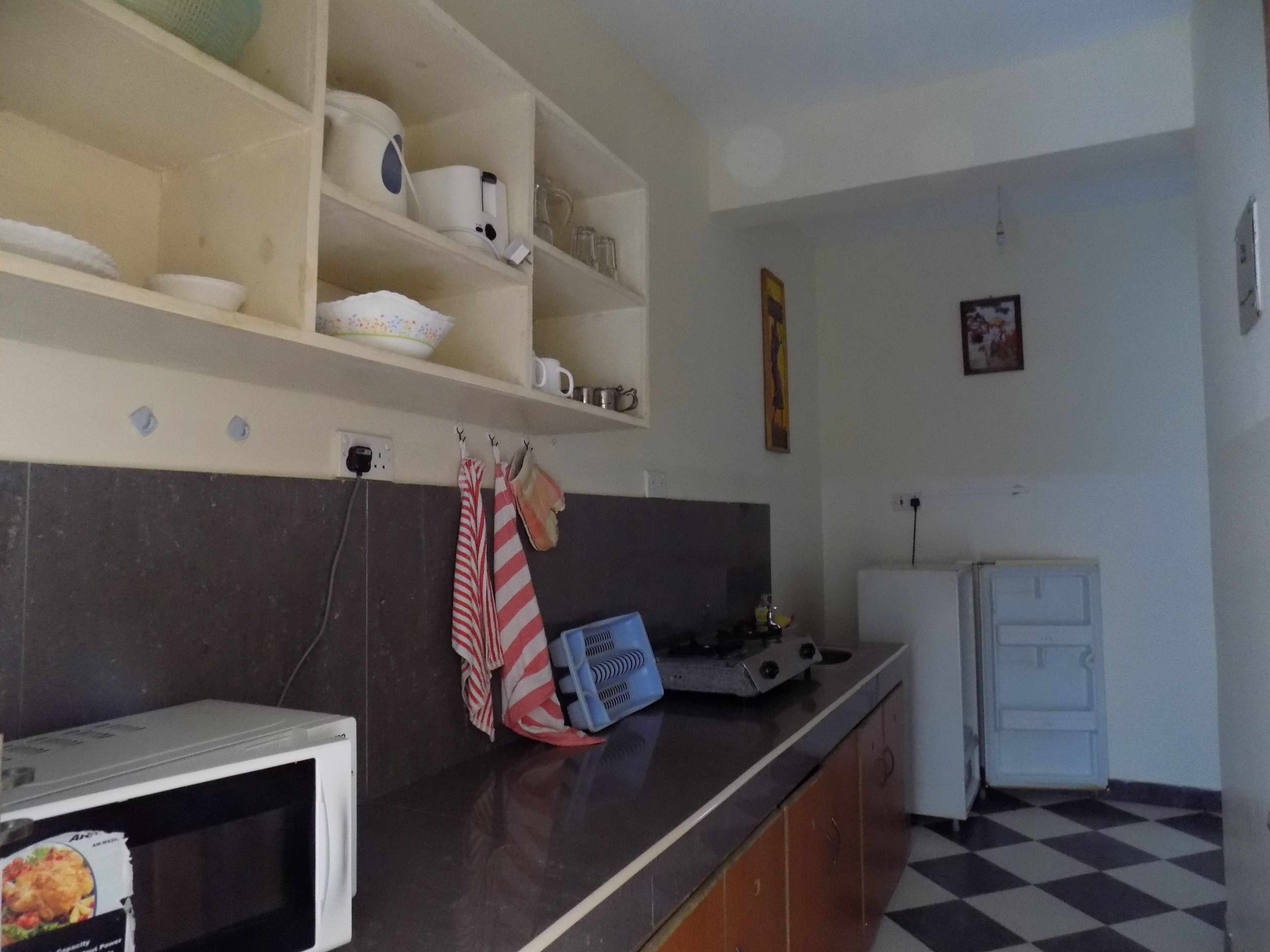 Une cuisine équipée d’un four à micro-ondes, d’une cuisinière et d’un évier. Des étagères au-dessus du plan de travail servent à ranger la vaisselle et les tasses. Une serviette est accrochée au mur.