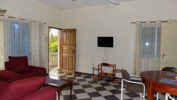 A room with a checkered floor, a red sofa, a wooden table, a TV mounted on the wall, and a balcony door.
