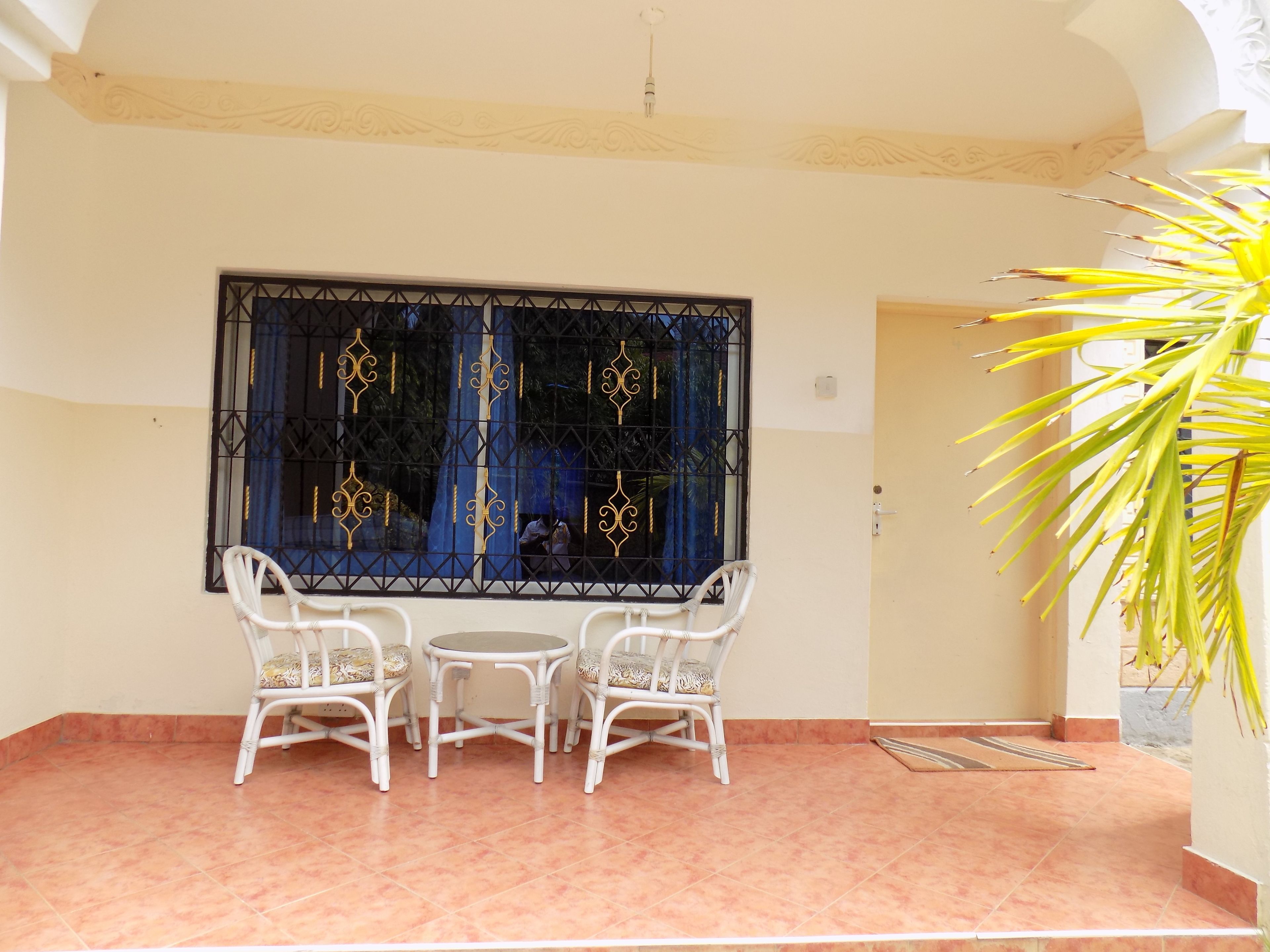 Una habitación con suelo de baldosas, una ventana con celosías decorativas y una planta en maceta.