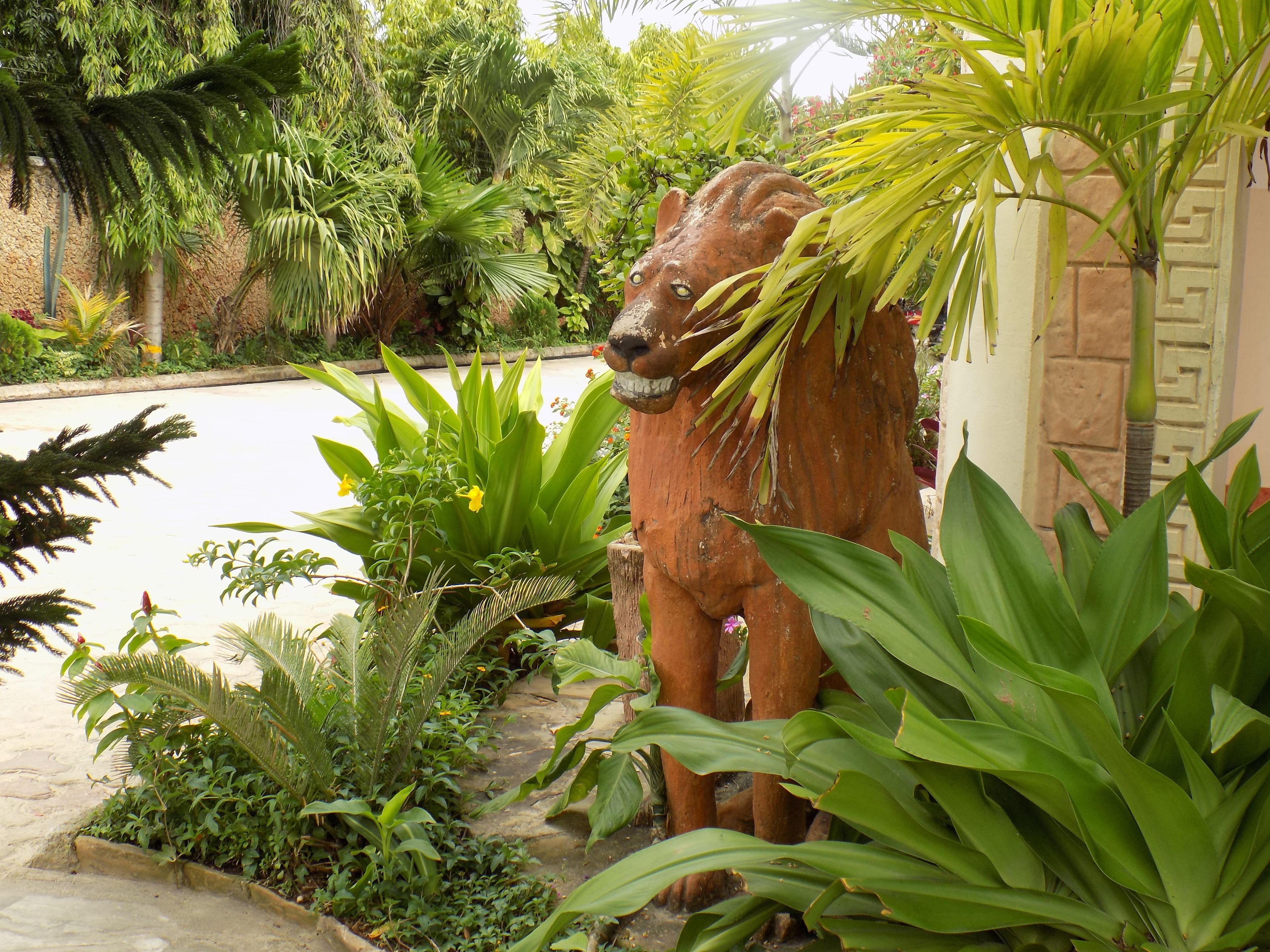 Un giardino con una grande statua di elefante dallo stile rustico, circondata da vegetazione lussureggiante e piante.