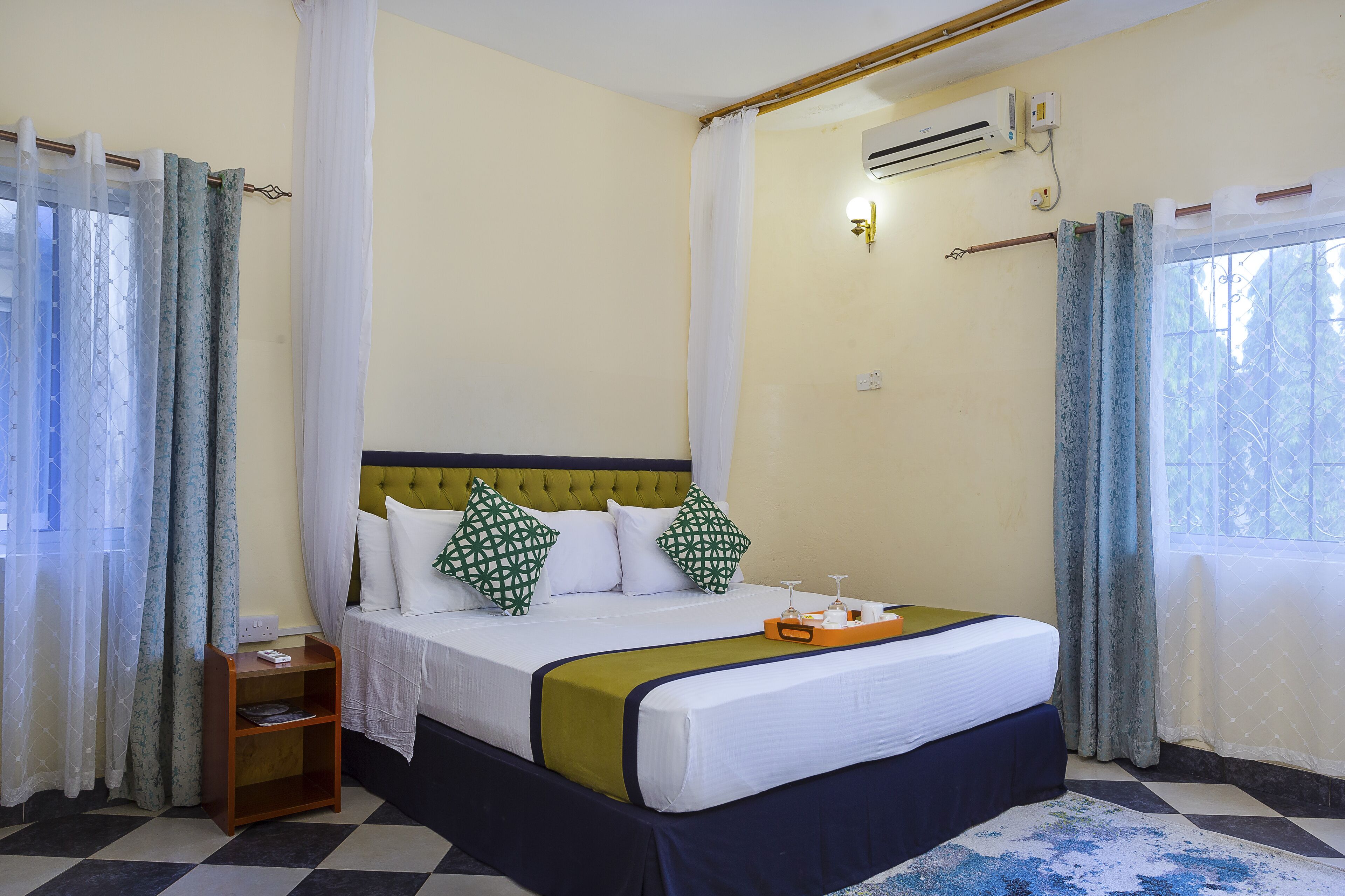 A hotel room with a bed, a nightstand, a window with curtains, and an air conditioning unit.