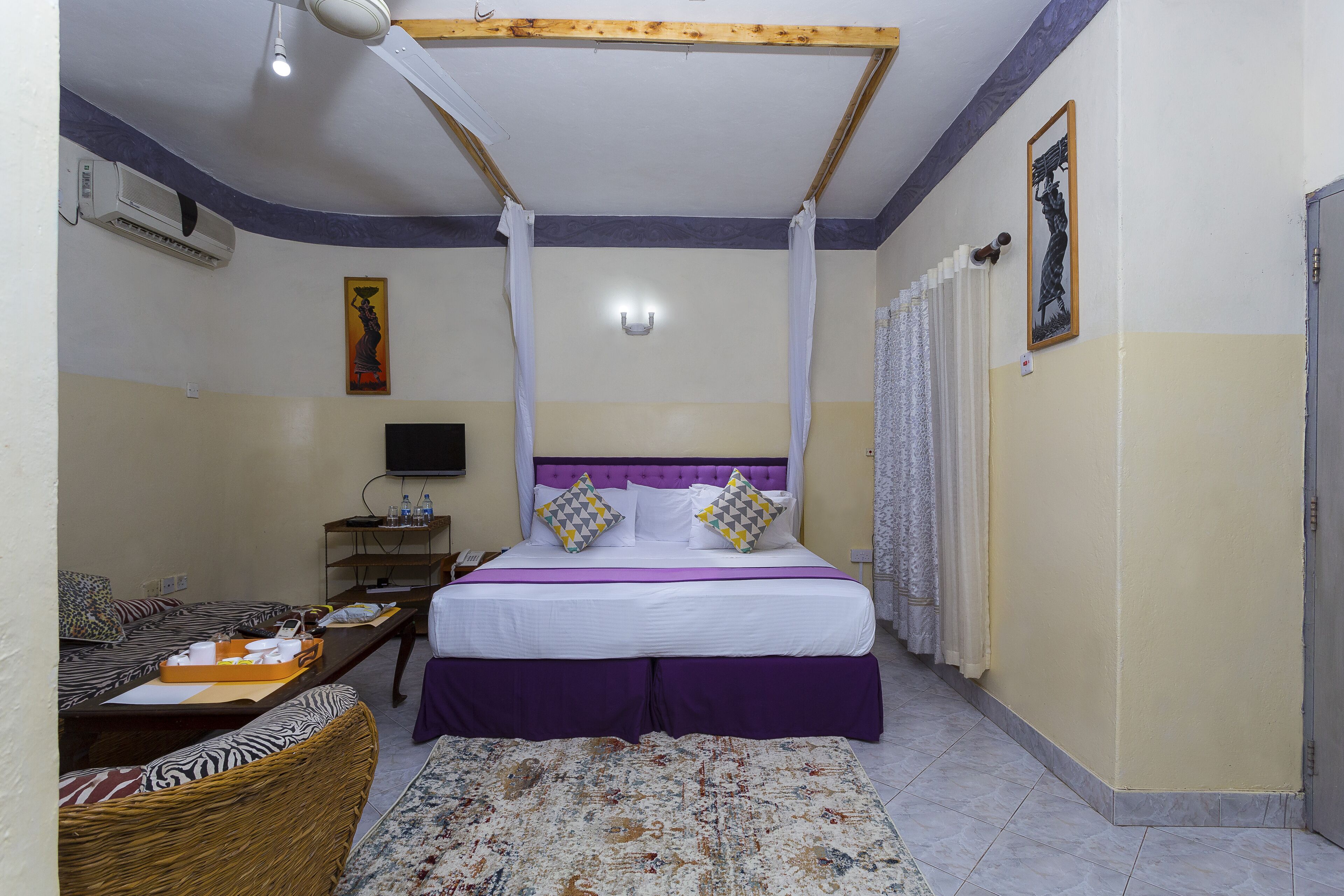 A bedroom with a bed, a sofa, a television, and a wall-mounted air conditioner.