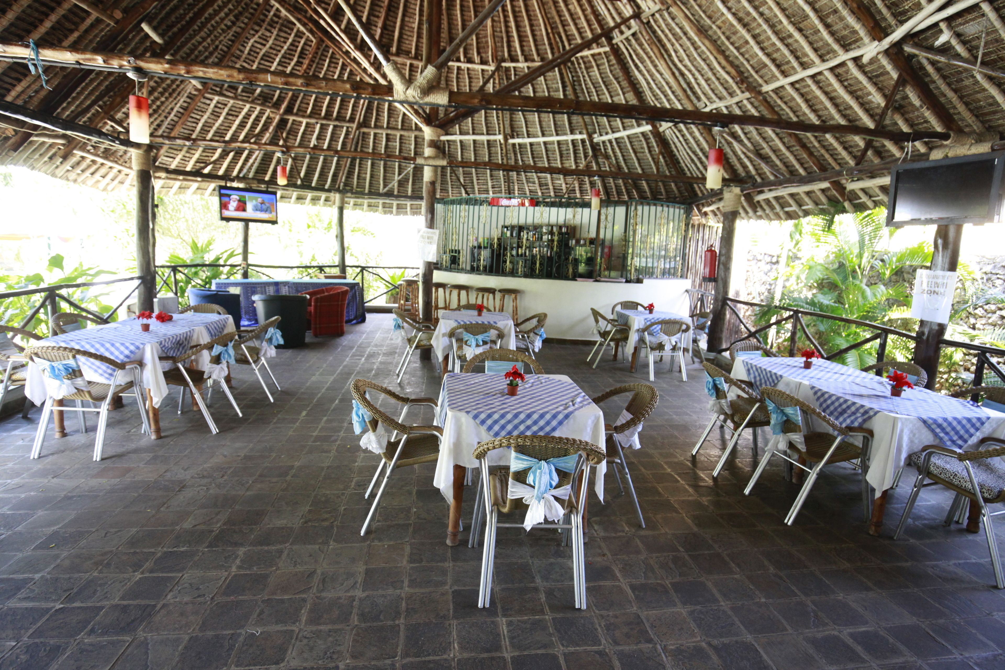 Een openluchtrestaurant met tafels en stoelen, een bar en een rieten dakconstructie.