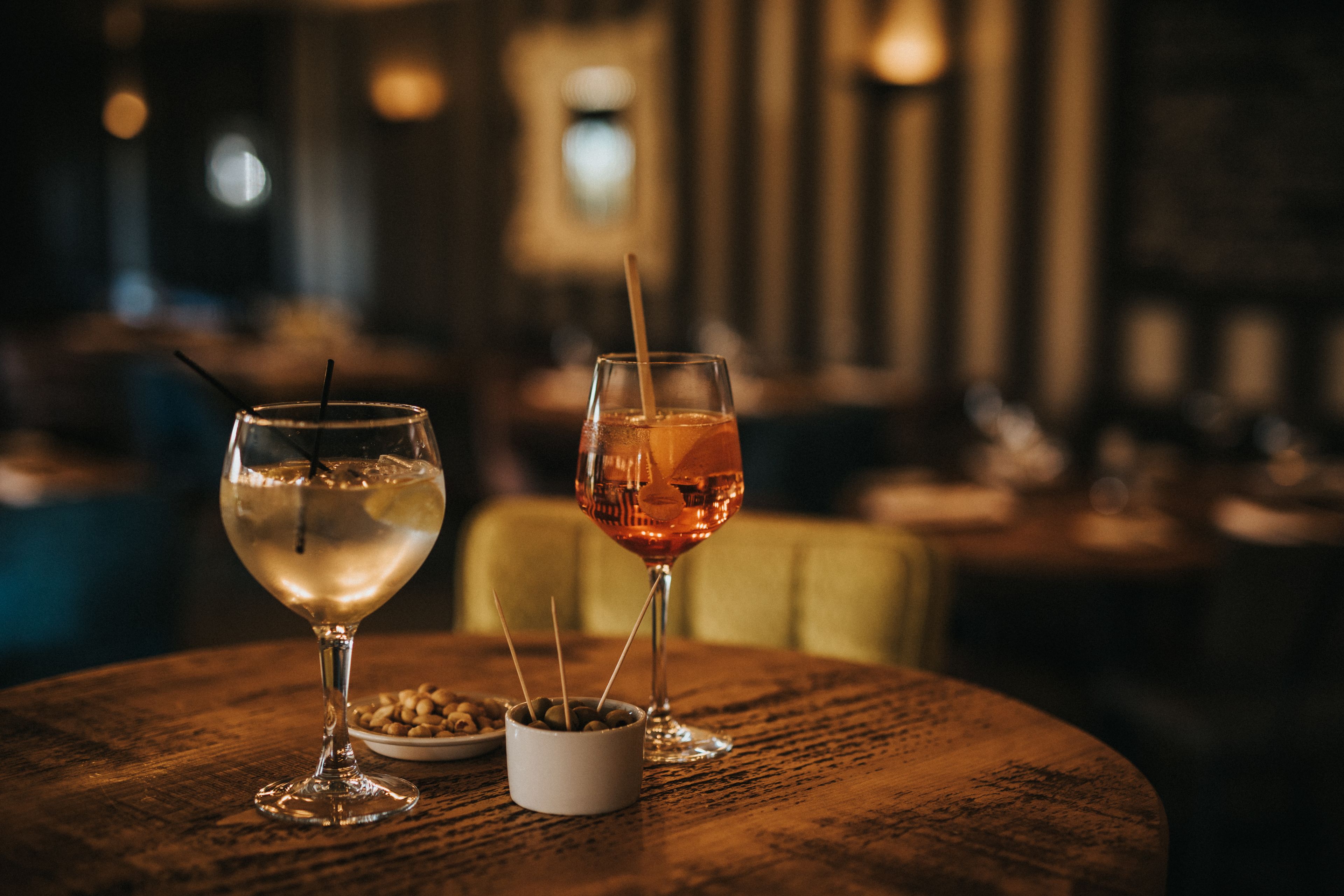 Dos vasos de bebidas sobre una mesa redonda de madera con un cuenco pequeño de nueces.