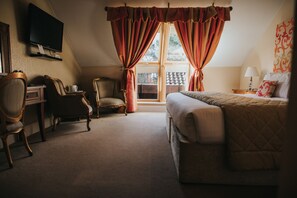 Ein Hotelzimmer mit einem Bett, einem Schreibtisch, einem Sessel, einem Fernseher und einem Fenster mit Vorhängen.