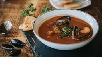 Un tazón de sopa de mariscos con mejillones, adornado con hierbas, sobre una tabla de pizarra.