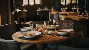 Uma mesa de jantar posta com pratos, copos e talheres, rodeada por cadeiras.