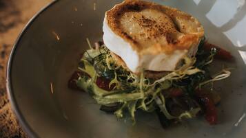 A plate with a piece of white fish, a golden-brown crust, and a bed of greens and red vegetables.