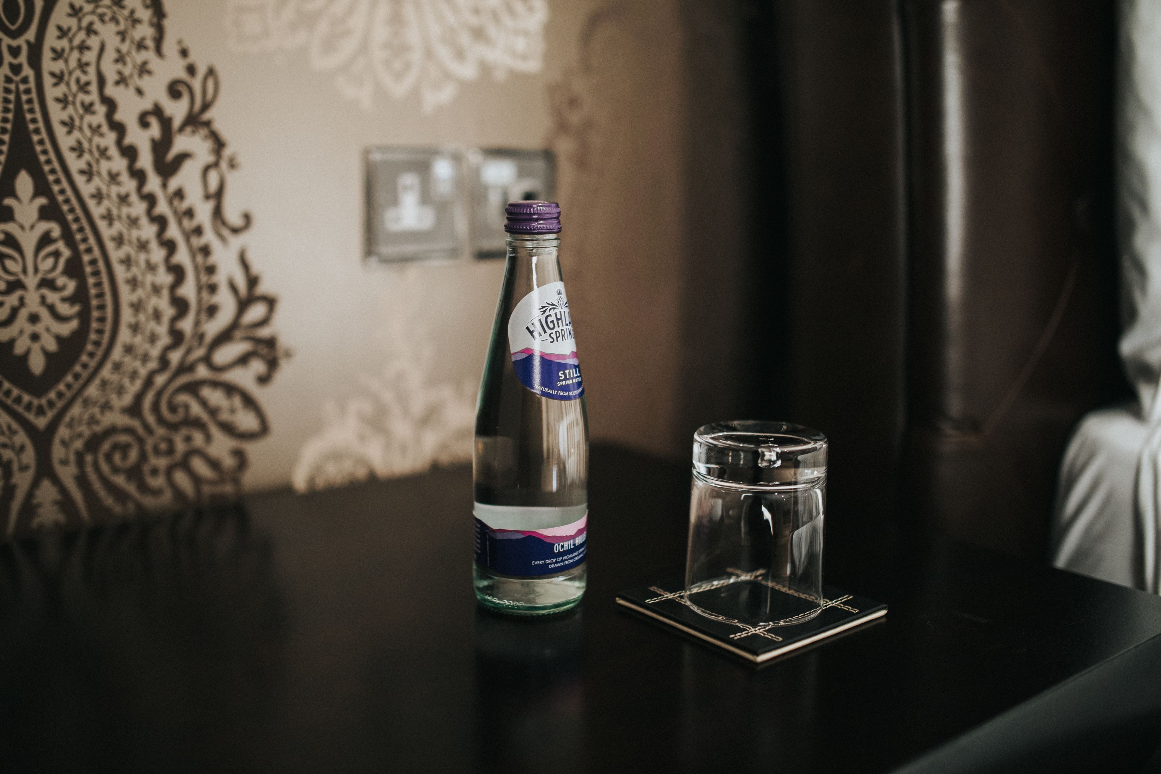A bottle of Kahlua on a table with a glass and a coaster.