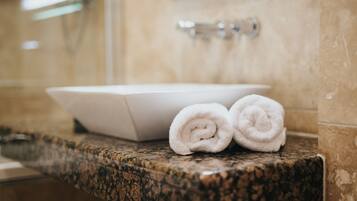 A bathroom with a marble countertop, a white sink, and two rolled towels.