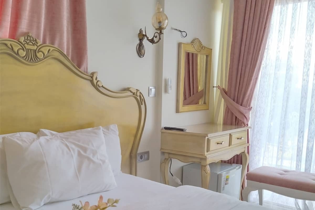 A hotel room with a bed, a vanity with a mirror, a small table, and a window with curtains.