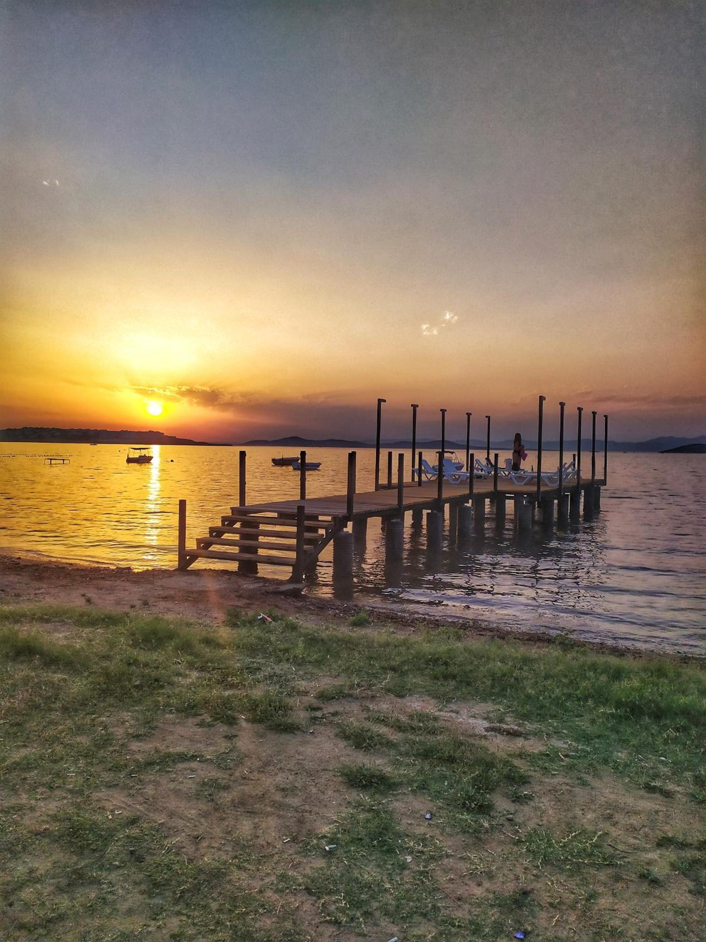 Une jetée en bois s’étendant sur une étendue d’eau calme au coucher du soleil.
