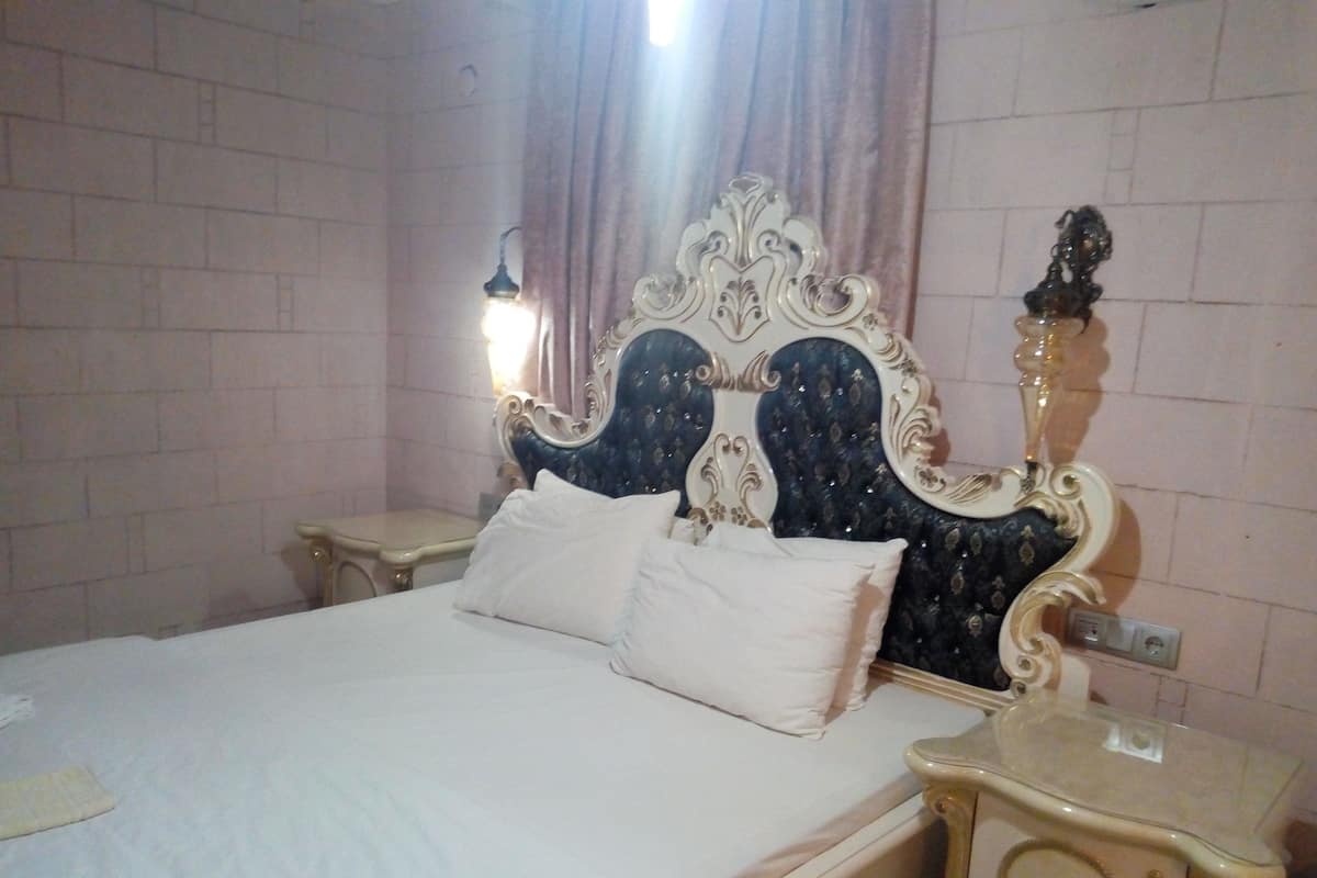 A bed with ornate headboard, two bedside tables, and a wall-mounted light fixture.