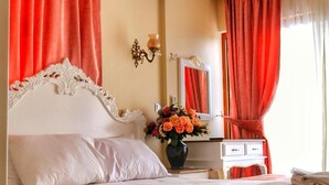 Een slaapkamer met een groot bed, een nachtkastje met een bloemenvaas, een dressoir en een spiegel.