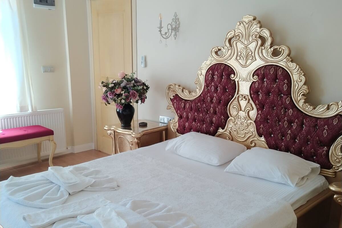 A neatly made bed with white linens and towels, a decorative vase with flowers, and a classic ornate headboard.