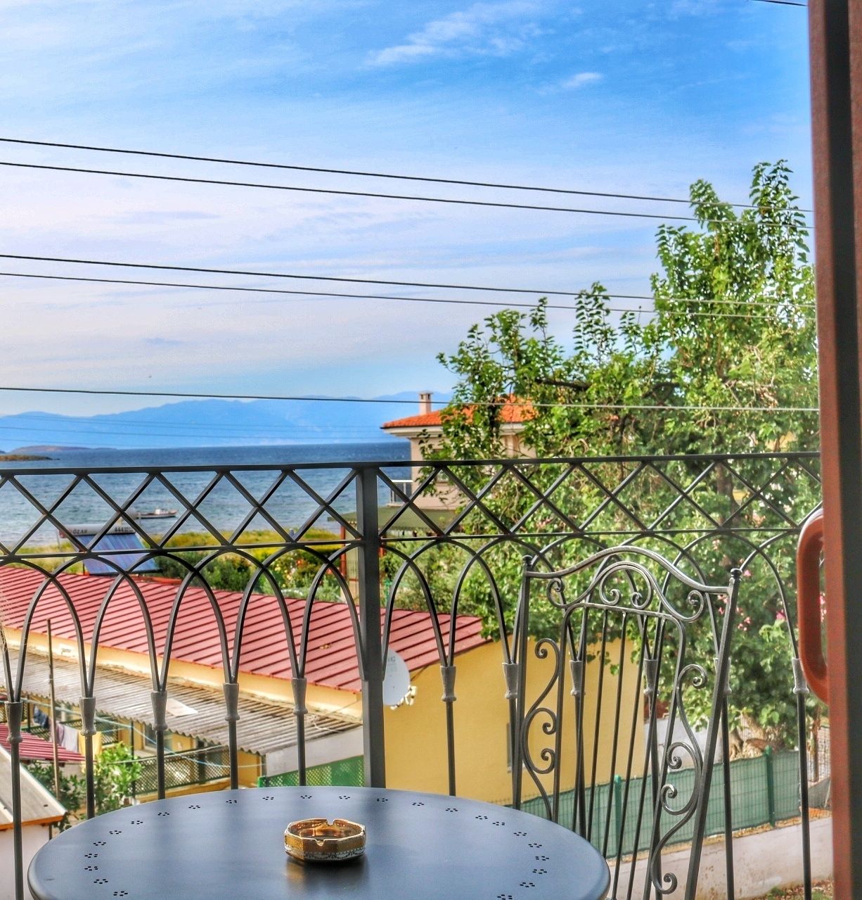 Uma varanda com vista para o mar, corrimão de metal e uma mesa com uma tigela.
