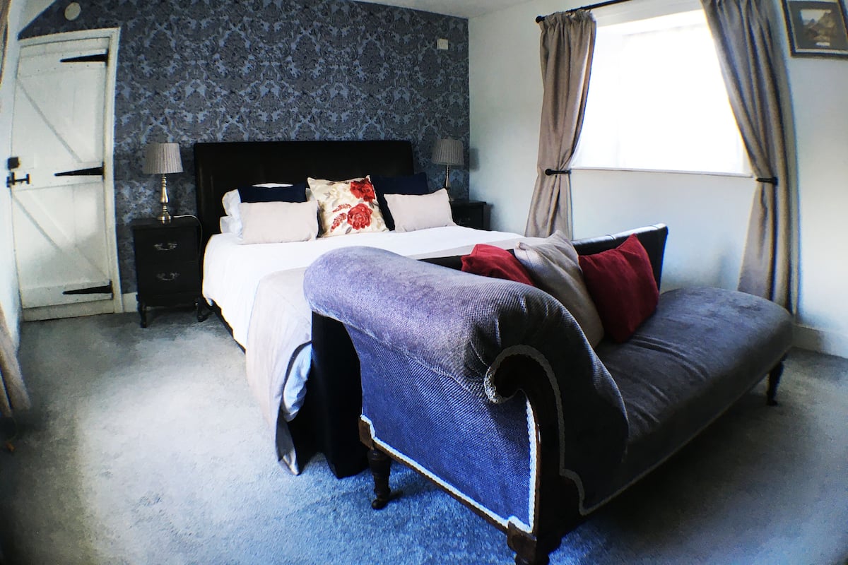 A bedroom with a bed, a nightstand, a lamp, a window with curtains, and a door.