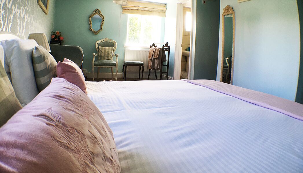 A bedroom with a large bed, a chair, a window, and a mirror.