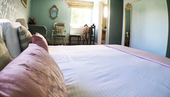 Un dormitorio con una cama grande, una silla, un ventanal y un espejo.