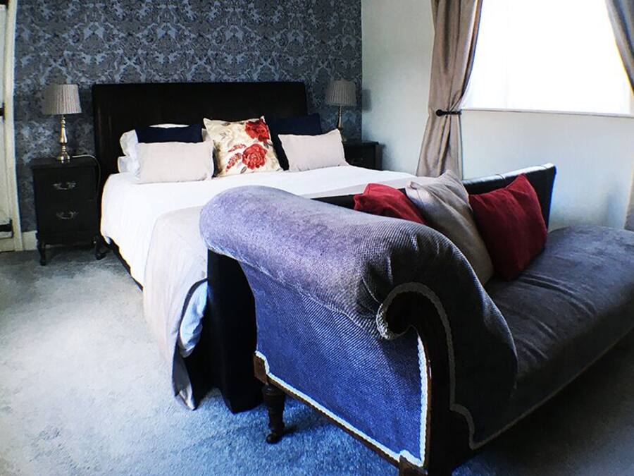 Un dormitorio con cama, mesitas de noche, un ventanal con cortinas y un sofá.