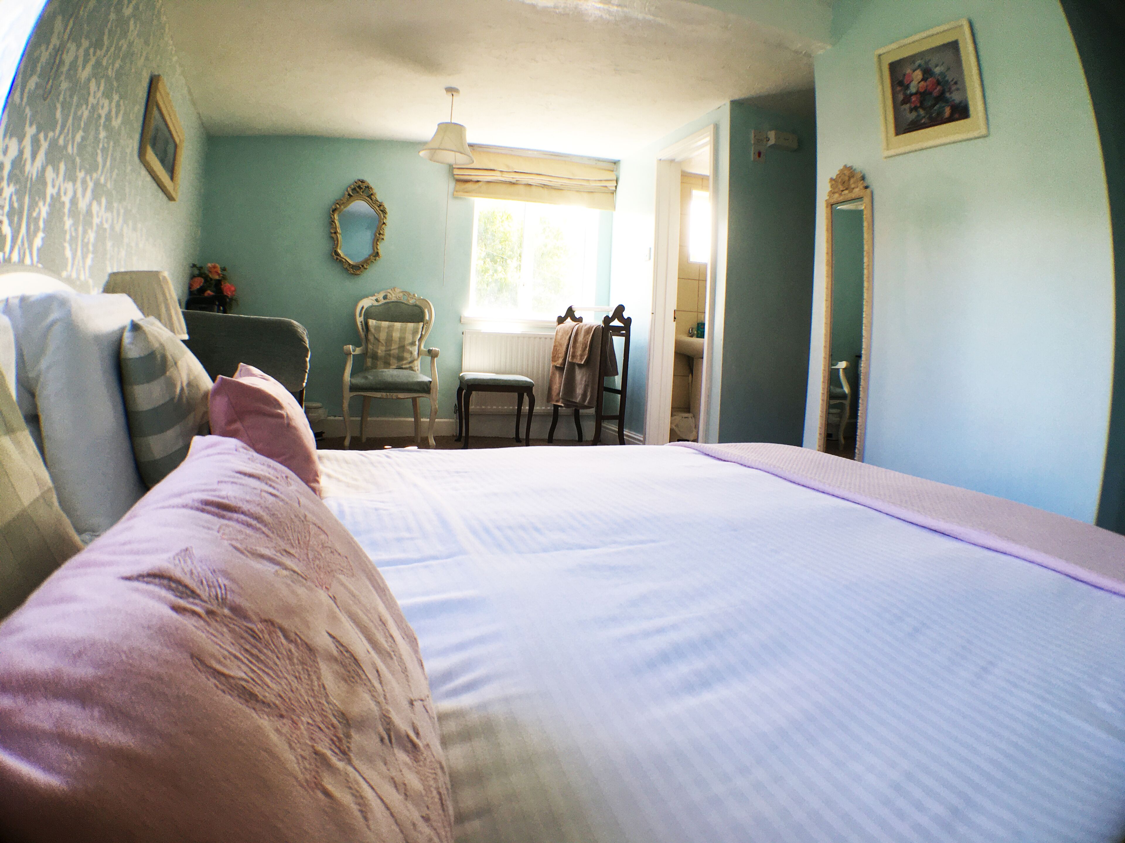 A bedroom with a large bed, a chair, a table, and a window with a view of the outside.
