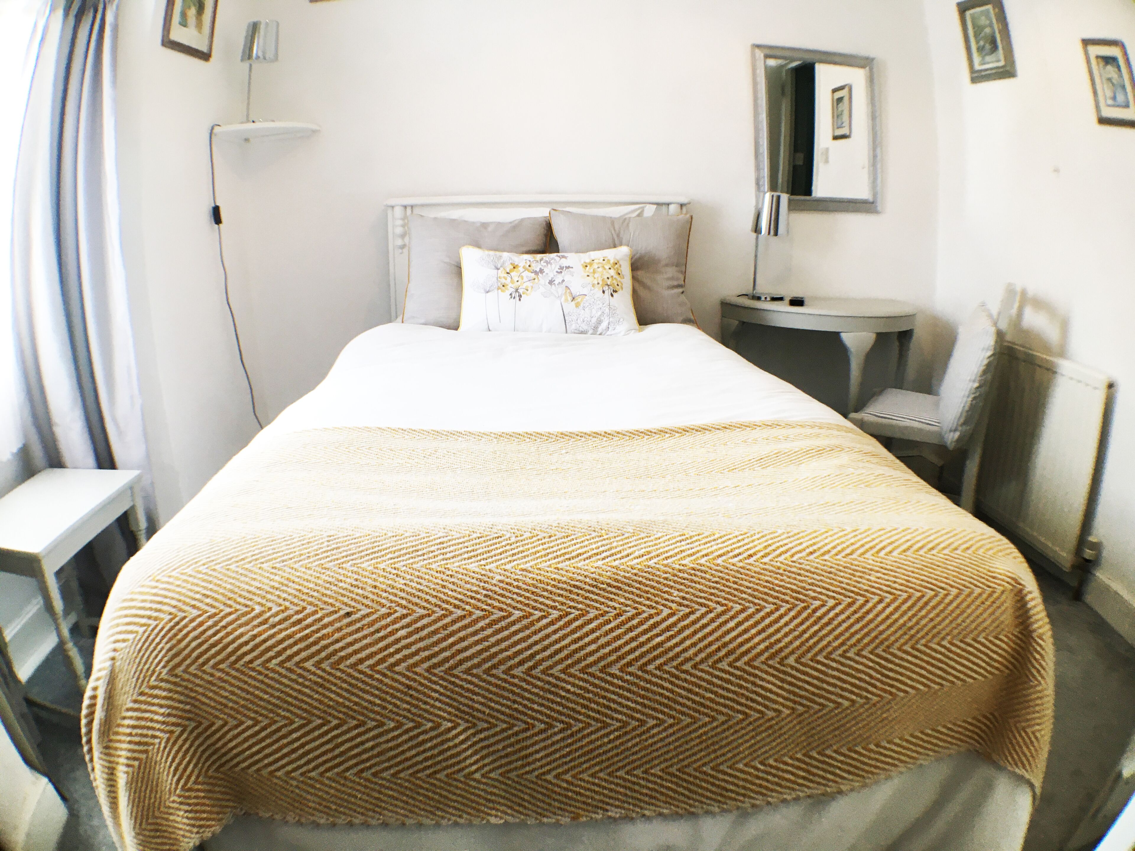 A hotel room with a bed, bedside table, and a mirror on the wall.