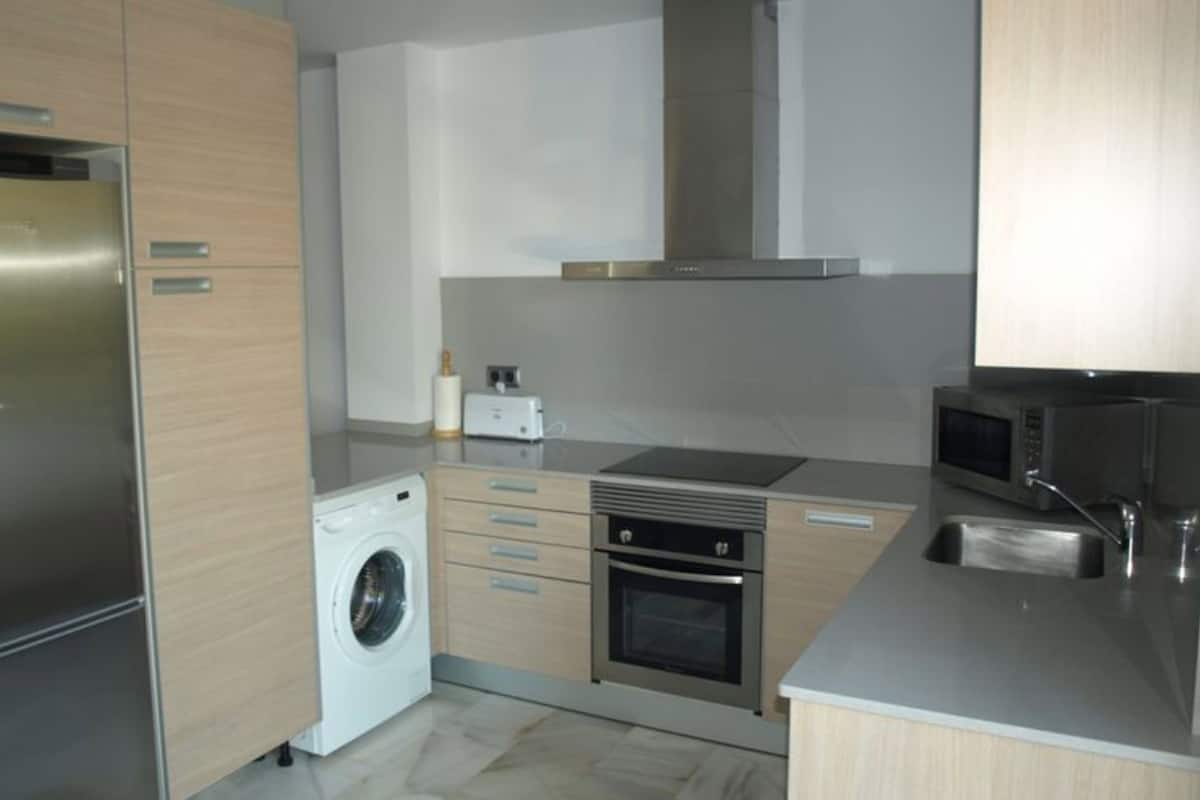 A modern kitchen with stainless steel appliances, wooden cabinets, a built-in washing machine, and a microwave.