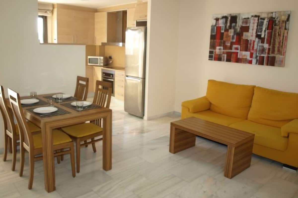 A modern living room with a yellow sofa, wooden dining table, and chairs.