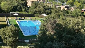 Una piscina con techo verde, rodeada de árboles y vista a un paisaje urbano al fondo.
