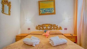 A hotel room with a bed, two bedside tables, a decorative headboard, a painting on the wall, and a window with curtains. - Albergo Antico Capon (Venice)