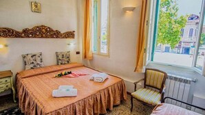 A hotel room with a bed, a chair, a window with curtains, a radiator, and a wall with a decorative headboard. - Albergo Antico Capon (Venice)
