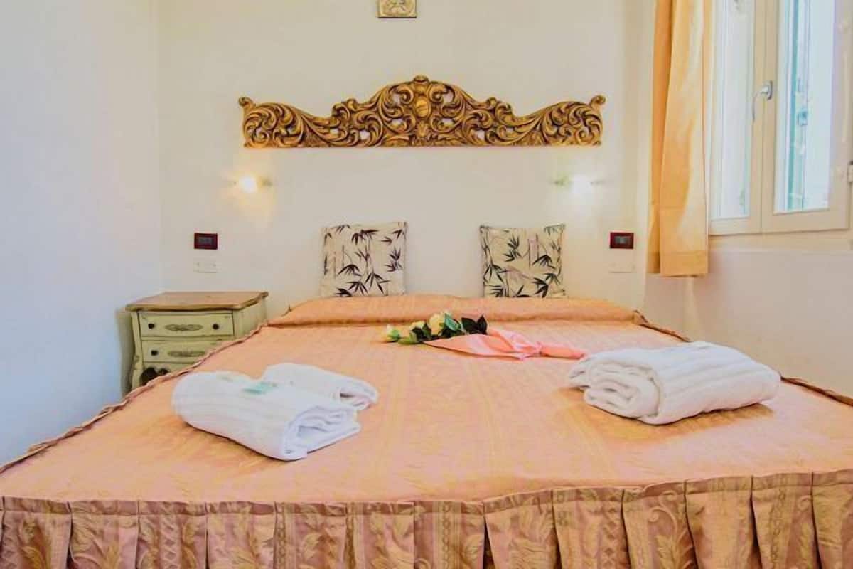 Un lit bien fait, avec deux serviettes pliées, une tête de lit décorative et une table de chevet avec une lampe.