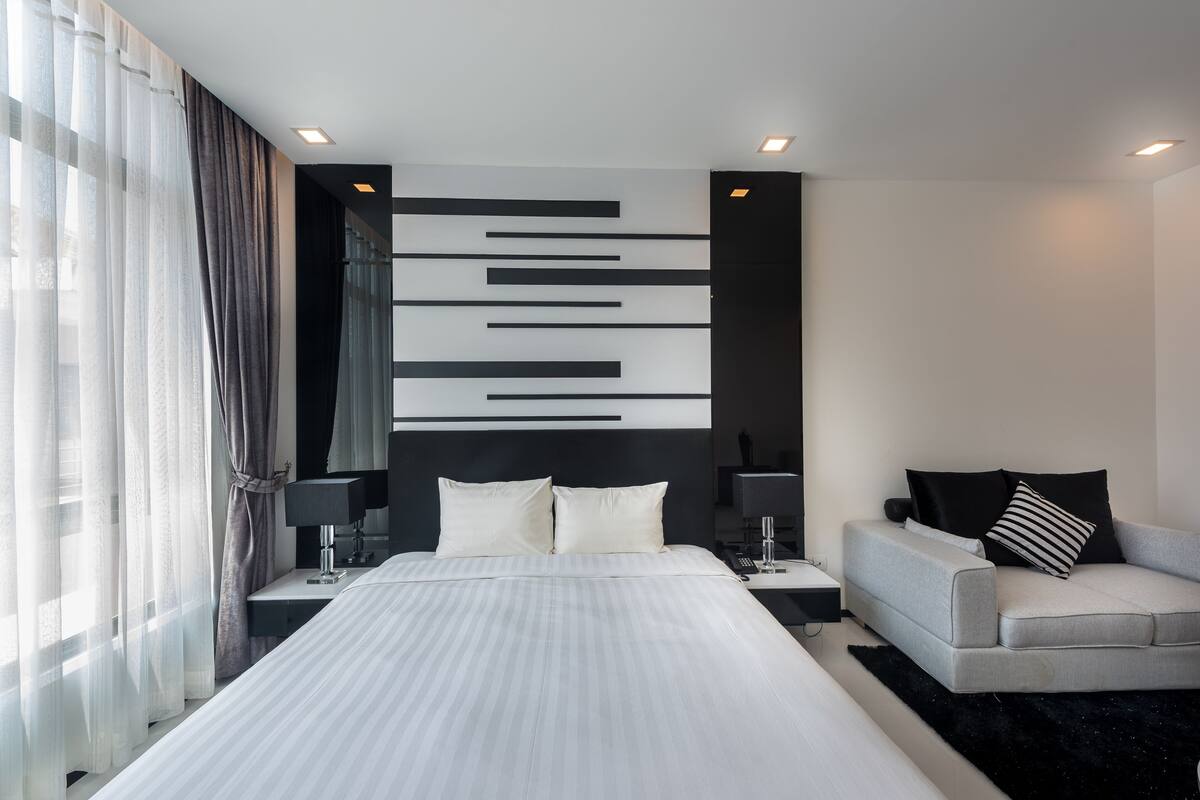 Une chambre d’hôtel moderne avec un grand lit, un canapé et un luminaire fixé au mur.