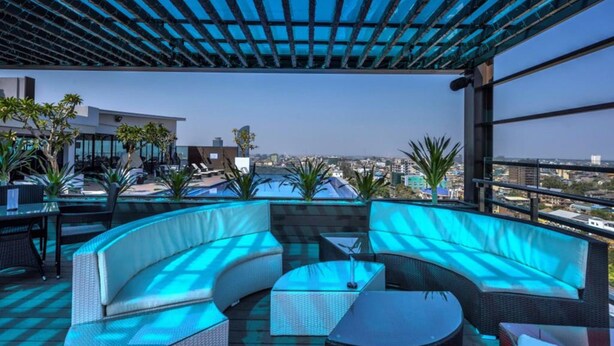 A rooftop lounge with a curved white sofa, a glass coffee table, and a view of the cityscape. - Maline Exclusive Serviced Apartments (Phnom Penh)