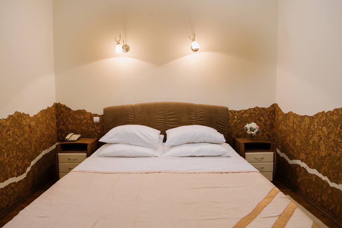 A neatly made bed with white linens and a brown headboard, two bedside tables with lamps, and a wall with a textured pattern.