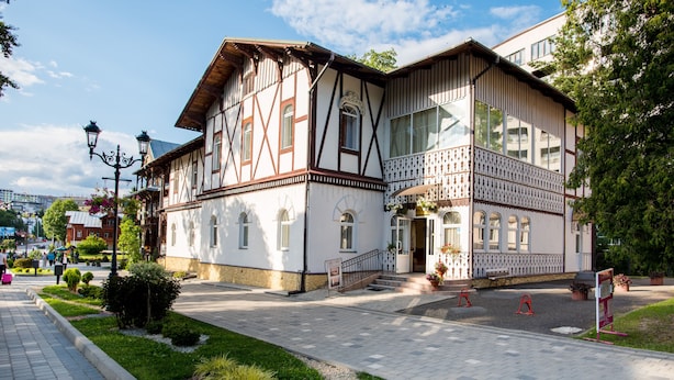 Un bâtiment traditionnel à colombages, doté d’un balcon, d’une allée pavée et d’un petit jardin.
