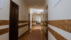 Un couloir avec des portes en bois, un sol recouvert de moquette et un mur de marbre orné d’un motif à rayures.