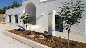 A building with a white exterior, blue doors, and a central arched entrance. There are potted plants and a stone vase in the foreground. - Antica Masseria Torre Mozza (Mesagne)