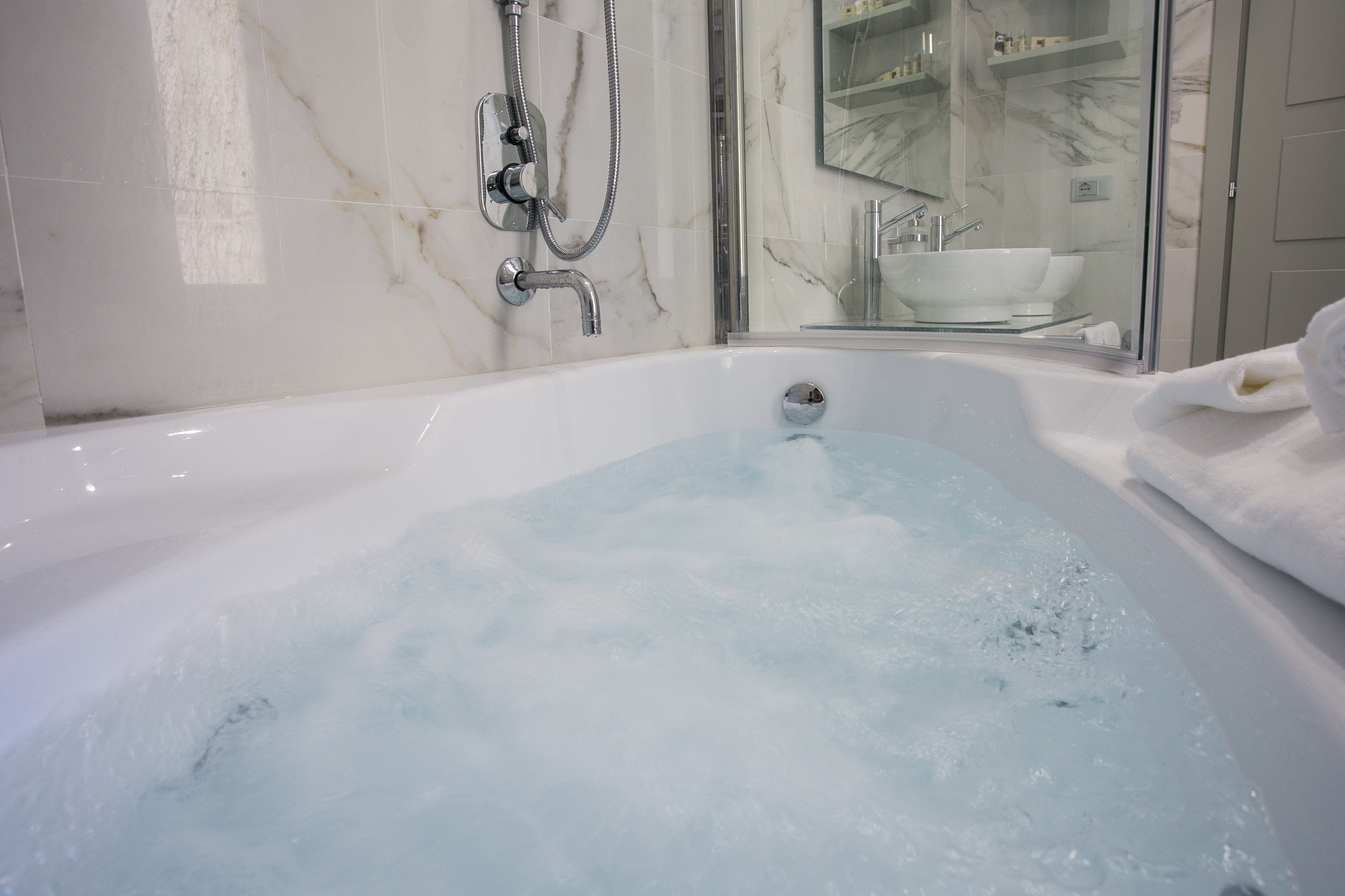 A modern bathroom with a large bathtub, a glass shower enclosure, and a marble-tiled wall.