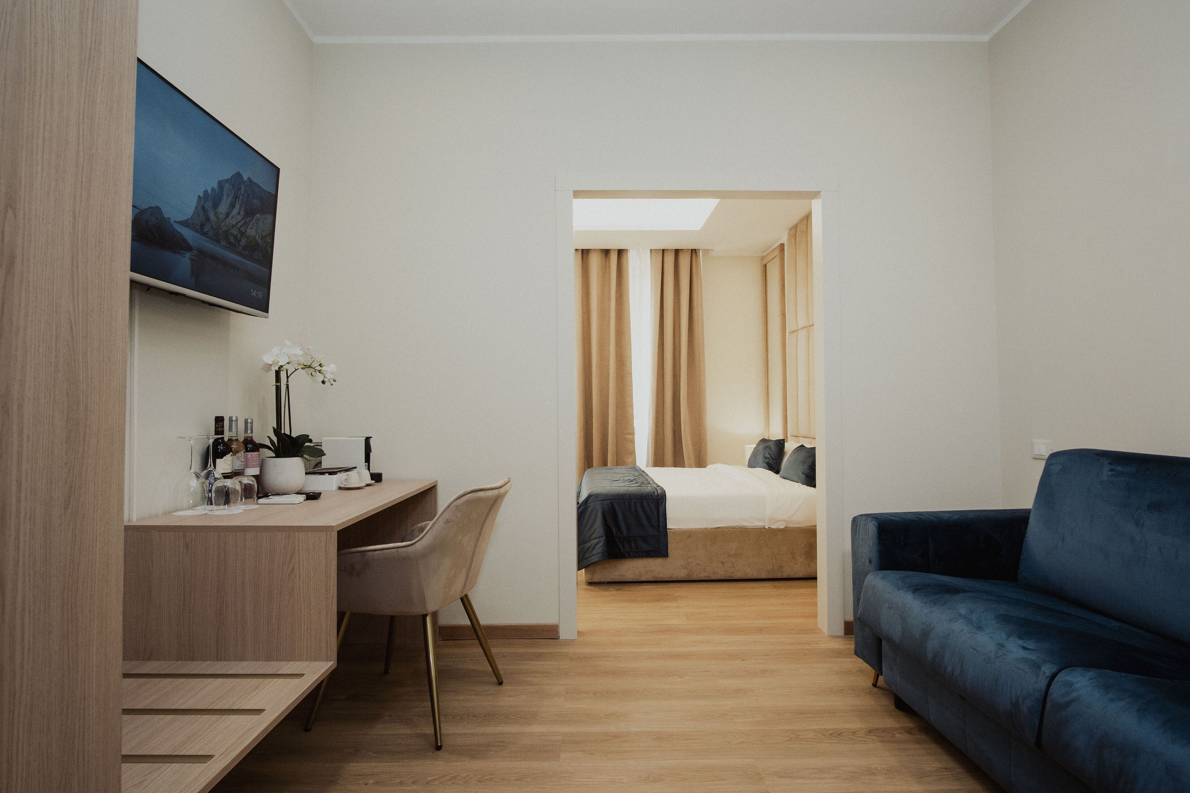 Una habitación de hotel moderna con un escritorio de madera, un sofá azul, una cama con colcha azul oscuro y un ventanal con cortinas.