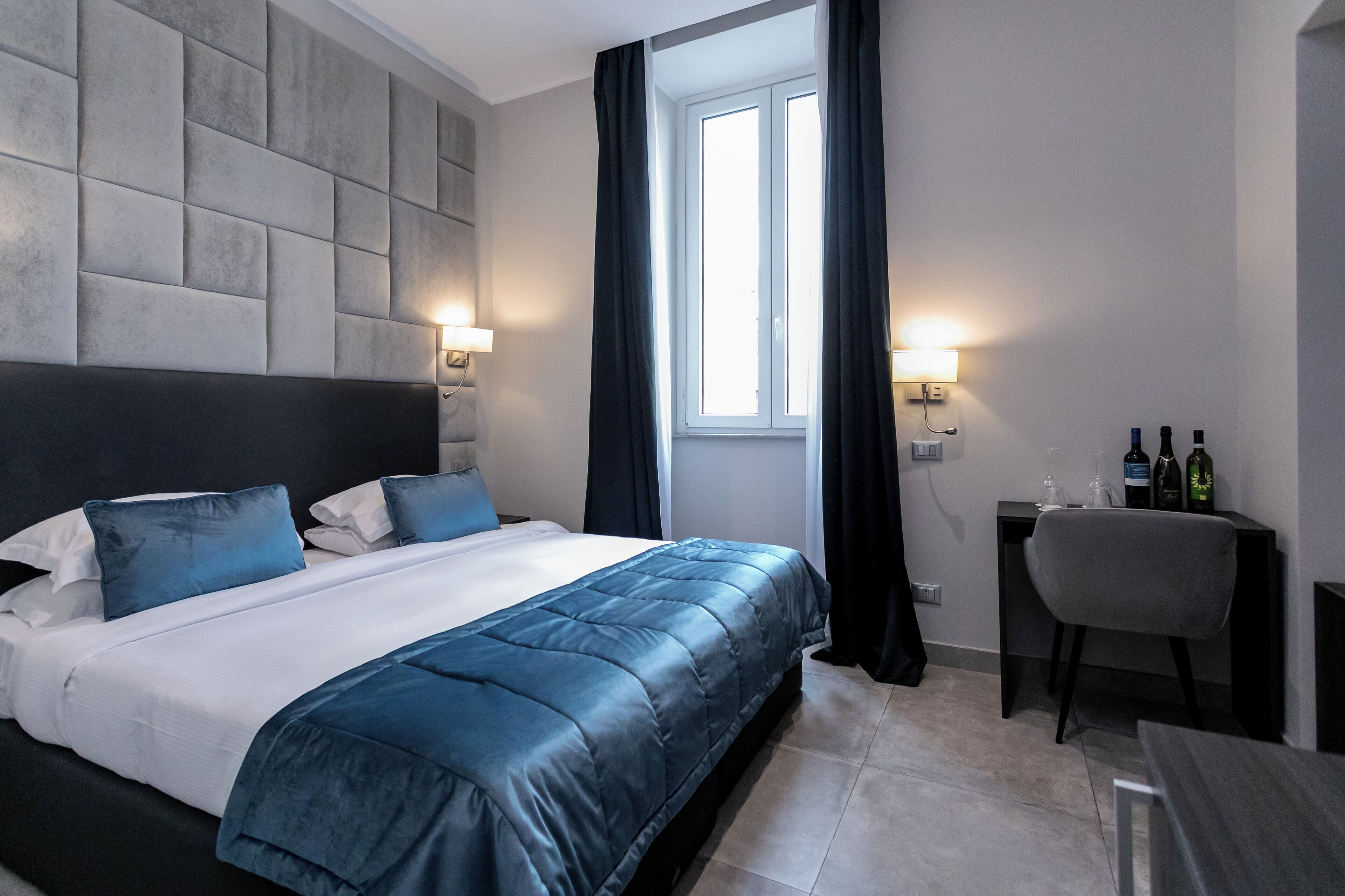 A modern hotel room with a large bed, a desk with a chair, and a window with curtains.